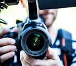 A close-up shot of a cameraman filming, focusing on the camera lens and equipment.